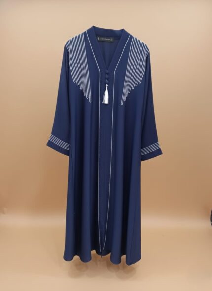 A woman wearing a navy blue abaya with white embroidered lines on the shoulders and down the front, featuring a white tassel at the V-neck.