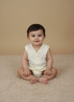 Three pastel baby sleeveless vests in cream, pink, and blue with front button closure, displayed on beige background.