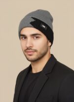 Grey ribbed beanie hat with black contrast detail and design patch on a neutral background.