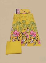 Unstitched 3-piece Maria B Lawn Suit fabric set. The shirt piece is yellow with large pink tropical flowers and green leaves. Includes a plain yellow bottom fabric and a top piece with a maroon patterned border.