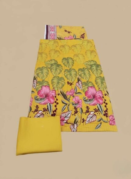 Unstitched 3-piece Maria B Lawn Suit fabric set. The shirt piece is yellow with large pink tropical flowers and green leaves. Includes a plain yellow bottom fabric and a top piece with a maroon patterned border.