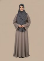Chic taupe abaya dress with intricate cut-out lace sleeves and a grey hijab, modeled by a smiling woman. A sophisticated modest fashion sweater.