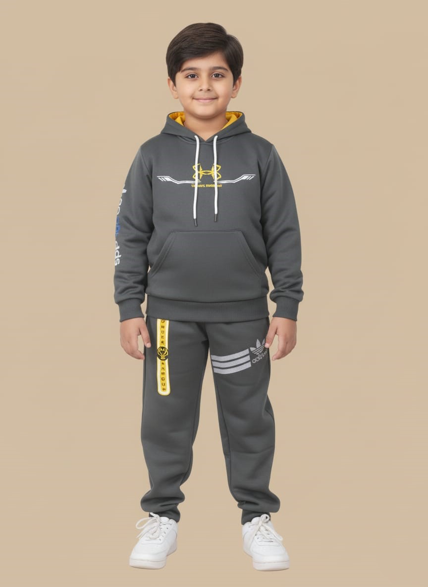 Boys Athletic Tracksuit | Grey Sportswear Set | Kids Activewear Happy boy in a grey athletic tracksuit with a yellow-lined hoodie and sports logos, matching joggers with stripes, and white sneakers, posing against a beige background.