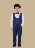 Full-length image of a young boy wearing a formal navy blue Kids Blue Suit Set with a white printed shirt and bow tie, standing against a beige background.