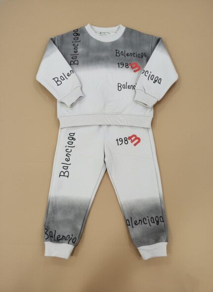 Flat lay image of a grey and white gradient Kids Tie-Dye Tracksuit, including a long-sleeve sweatshirt and joggers, both with "Balenciaga" branding and "1983" graphics.
