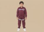 Happy boy in a maroon sports tracksuit with a zip-up jacket and striped joggers, featuring sports branding