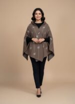 Taupe/mauve knit Capshwal (shawl-cape hybrid) with white geometric hashtag pattern and wide sleeves, draped on a light brown background.