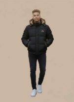 Main View: Gelani's black parachute jacket for men featuring a hooded puffer design and tan piping. Detail View: Close-up of the tan accent piping and side pocket detail on the men's black parachute jacket. Interior View: Black winter puffer jacket showing the contrasting tan hood lining and interior fabric. Hood Detail: Detachable insulated hood with snap-button closures on the men's winter parachute coat. Cuff & Hem: Reinforced elasticated cuffs and hem on the stitched parachute jacket for men. parachute jacket for men